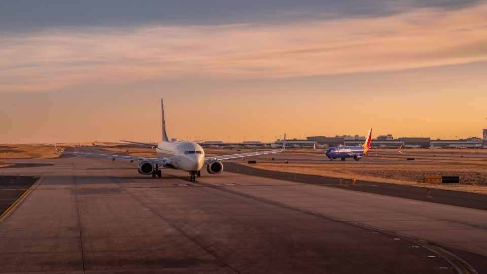 Aircraft taxiing on the runway at sunset, preparing for takeoff at a busy airport.